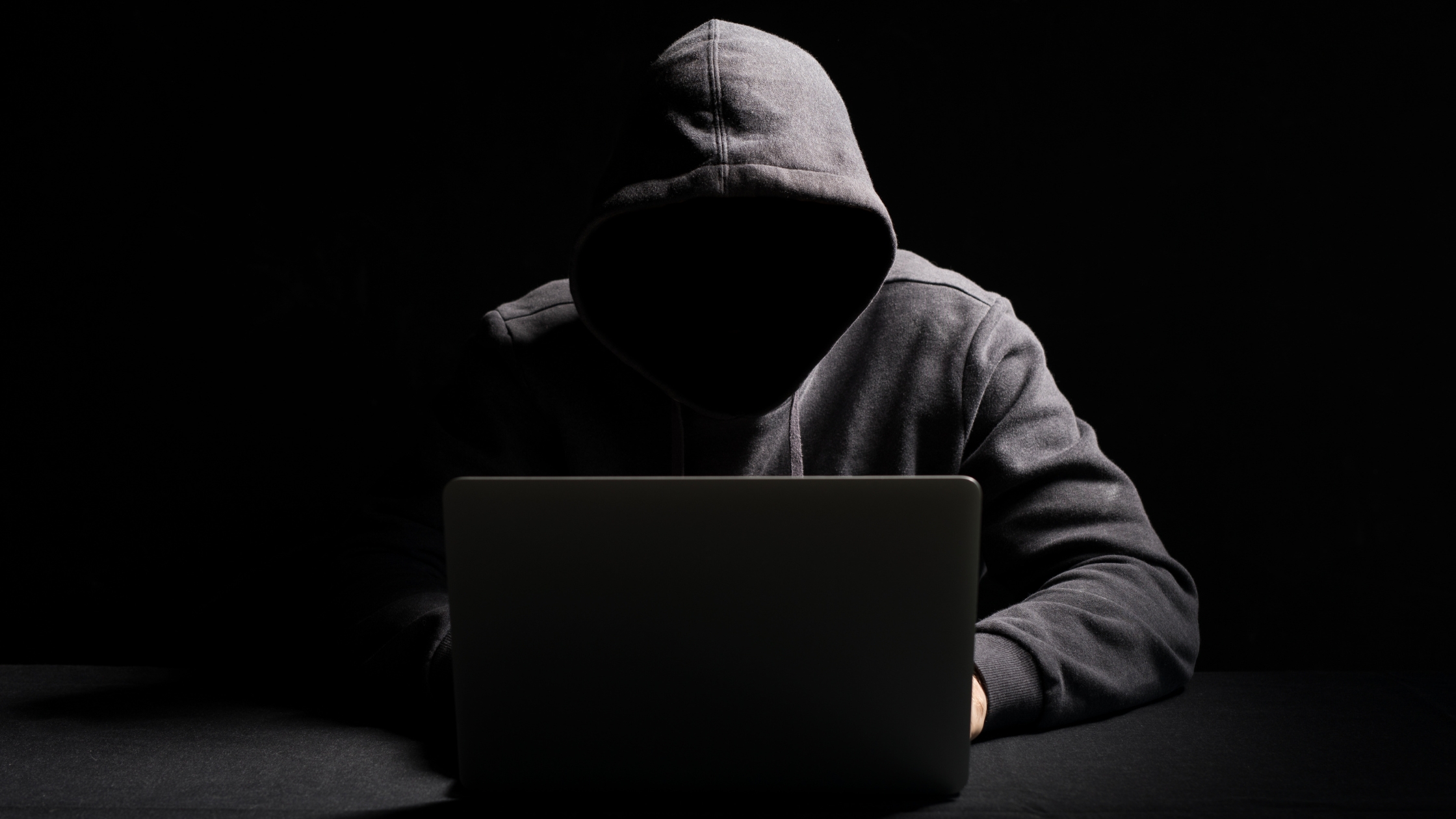 Hacker working on dark web threats on laptop in the dark